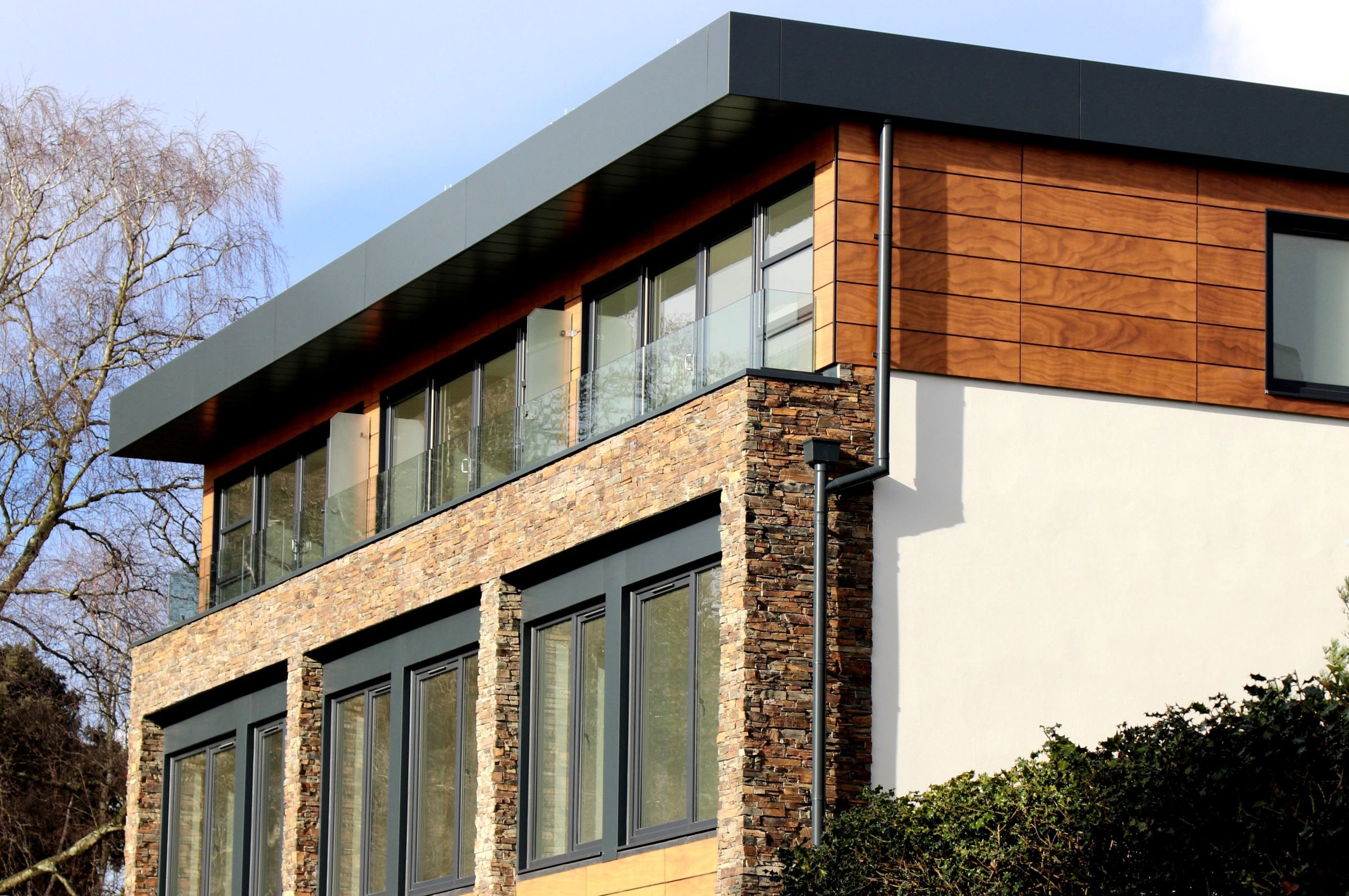 Taş ve ahşap kaplamalı, geniş pencereli iki katlı modern yapı
